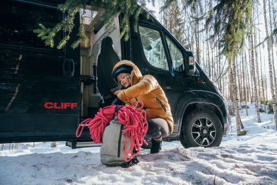 Kiipeilijä Anna Laitinen varusteineen auton edessä.
