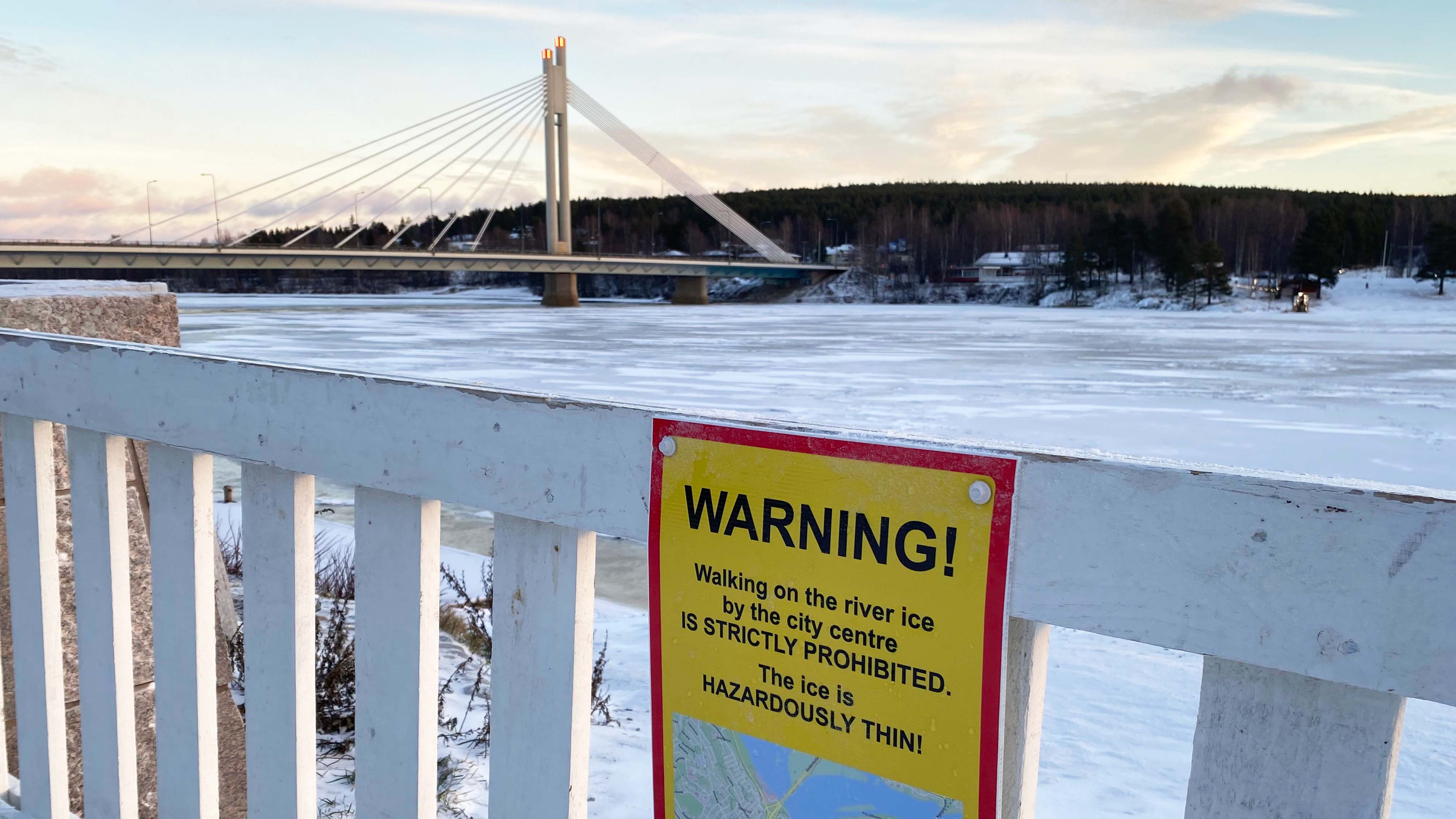 Kemijoen rannan asennetuissa aidoissa on erikielisiä kylttejä, joissa varoitetaan heikoista jäistä. Kuva. Rovaniemen kaupunki